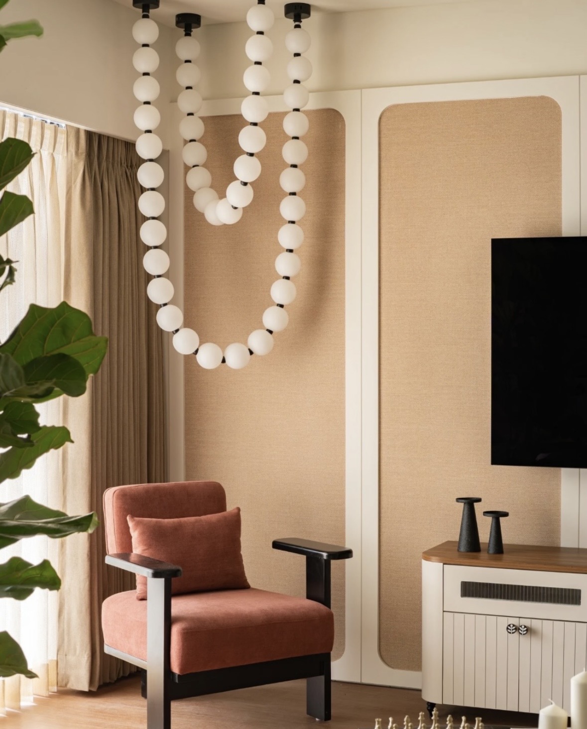 Glass-globe pendant hanging over a coral armchair, beside woven fabric panels and a white television unit