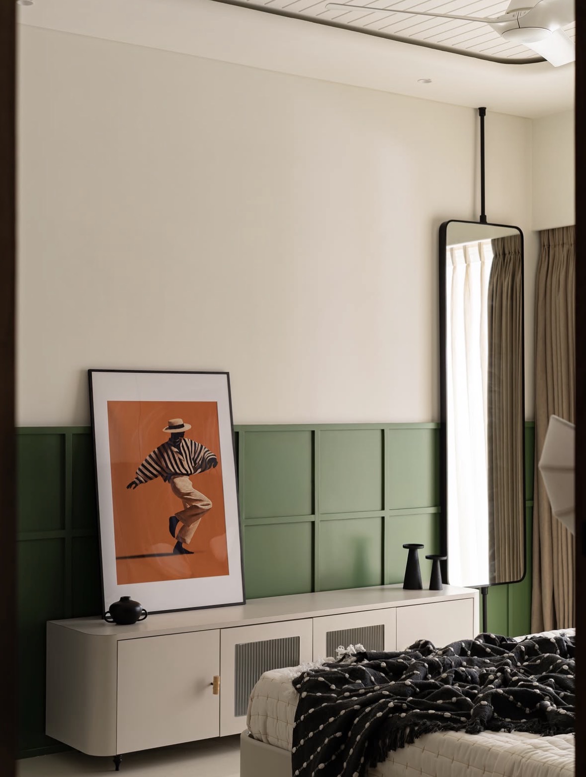 Framed artwork of a dancer in a striped shirt on a cabinet, beside a ceiling-hung mirror and green panelling
