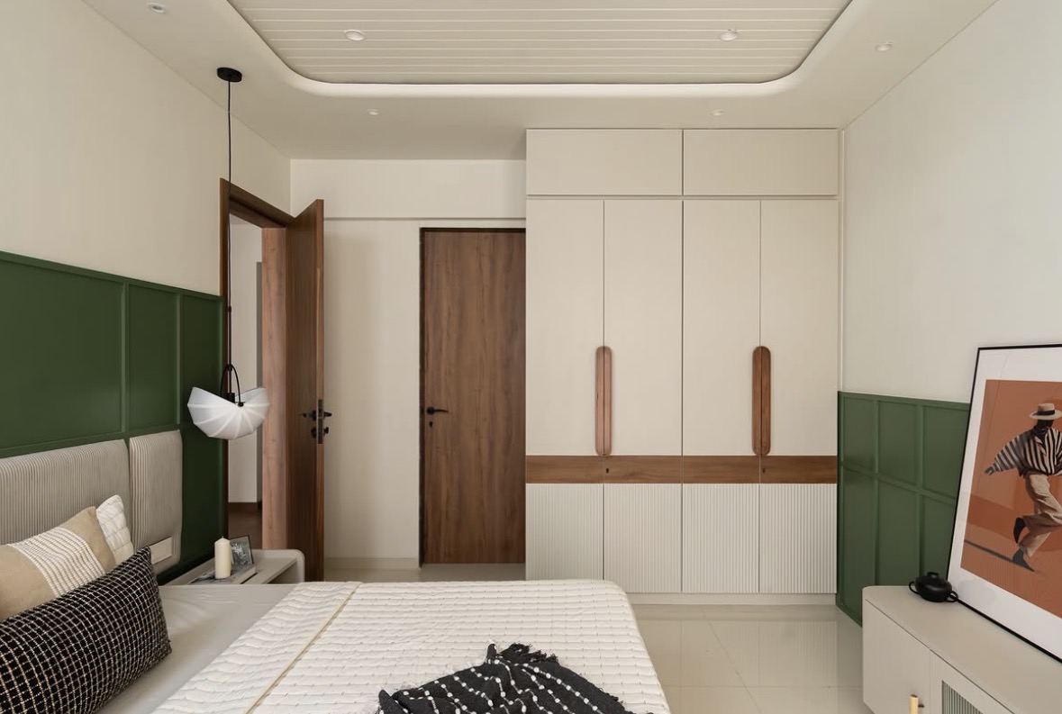 Bedroom with deep green panelling, a striped headboard, a white fitted wardrobe with carved timber handles and a framed artwork