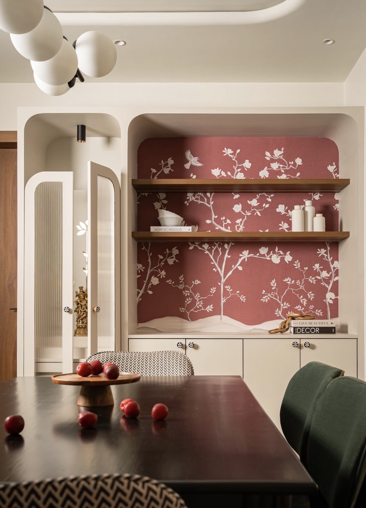 Rounded niche with pink floral wallpaper and open shelves, beside a reeded-glass cabinet that holds a small brass figure