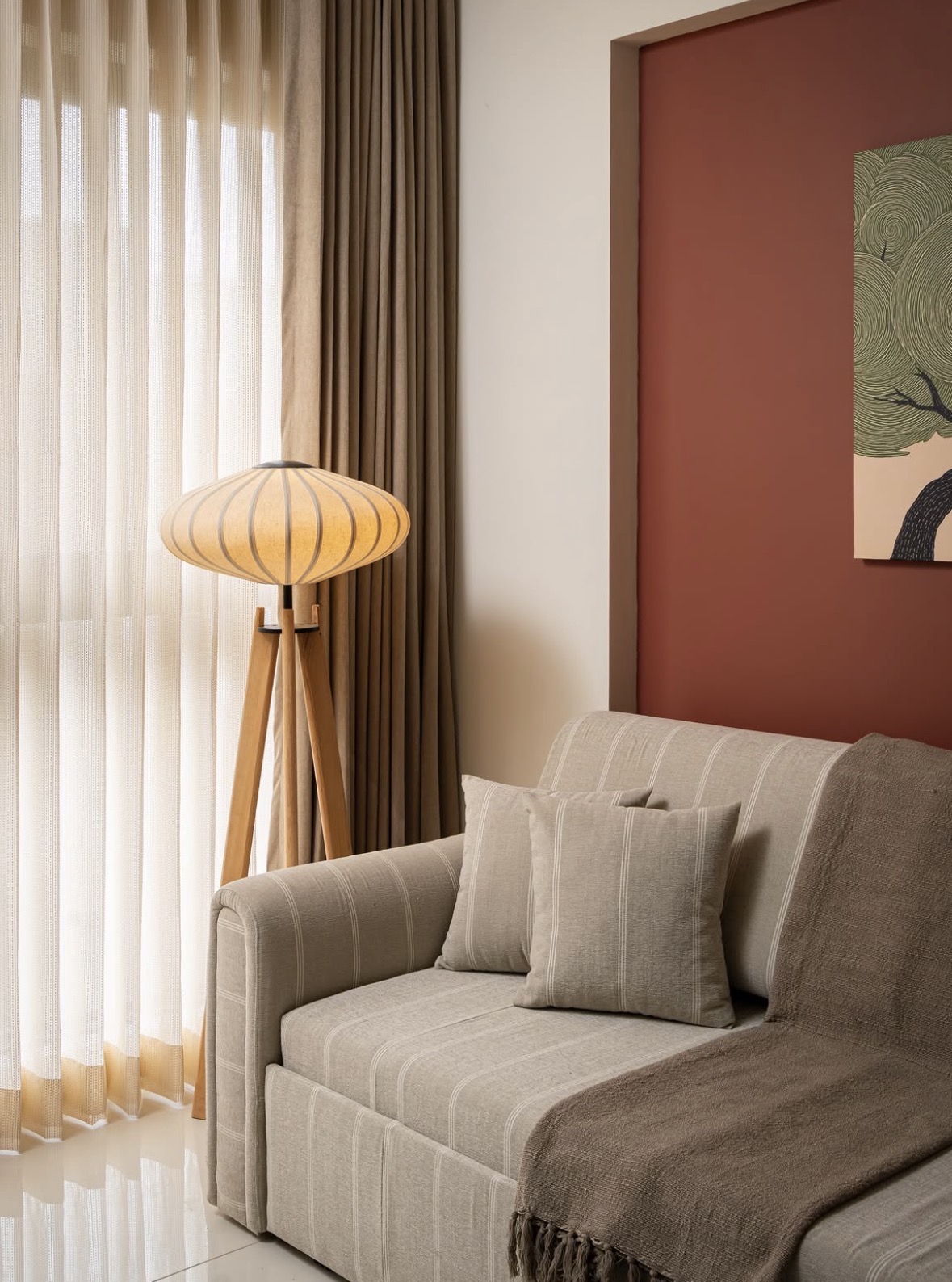 Striped sofa beside a tripod floor lamp and sheer and heavy curtains, against a terracotta wall with a framed artwork