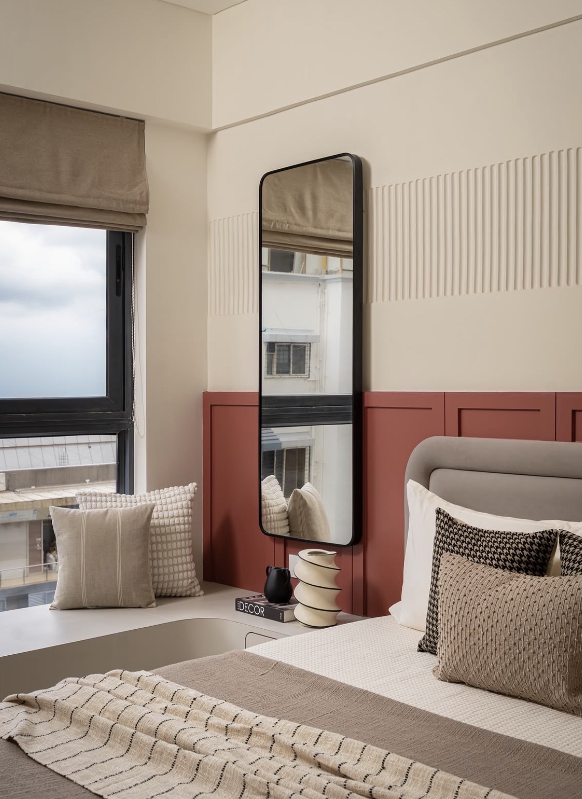Window seat and a tall black-framed mirror beside terracotta panelling and a ribbed plaster wall