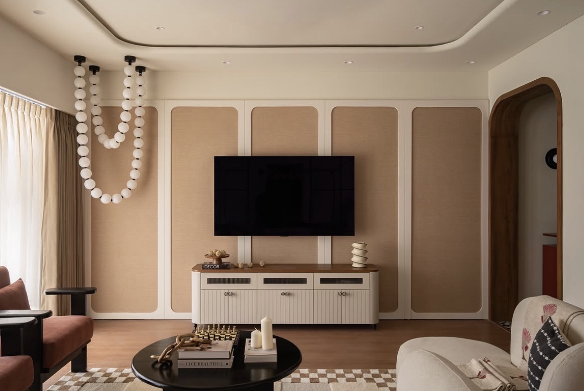 The finished living room: a woven-panelled wall, a wall-mounted television, a round black coffee table and a long string of white glass globes