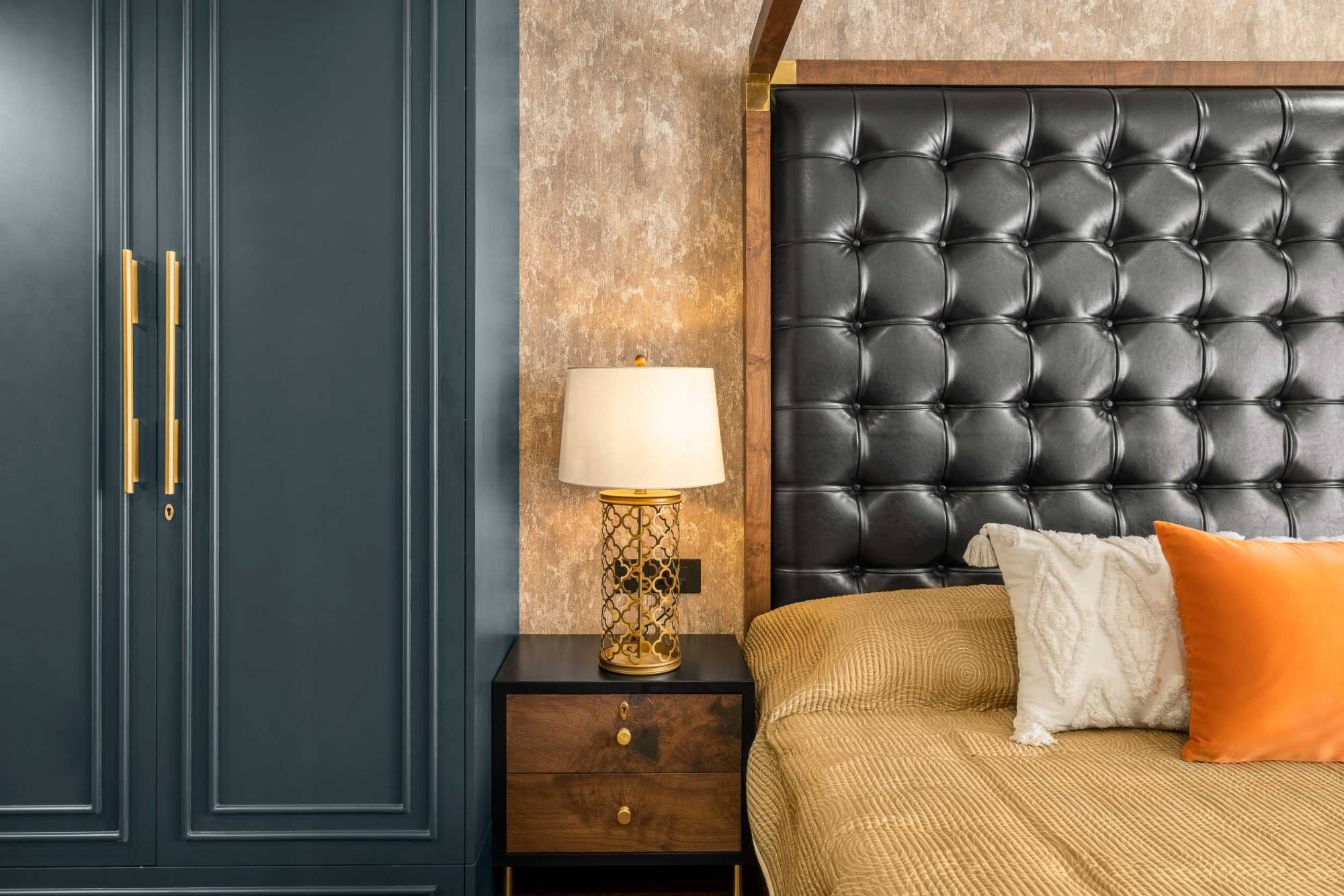 Brass openwork bedside lamp beside deep blue panelled wardrobe doors and a buttoned black headboard