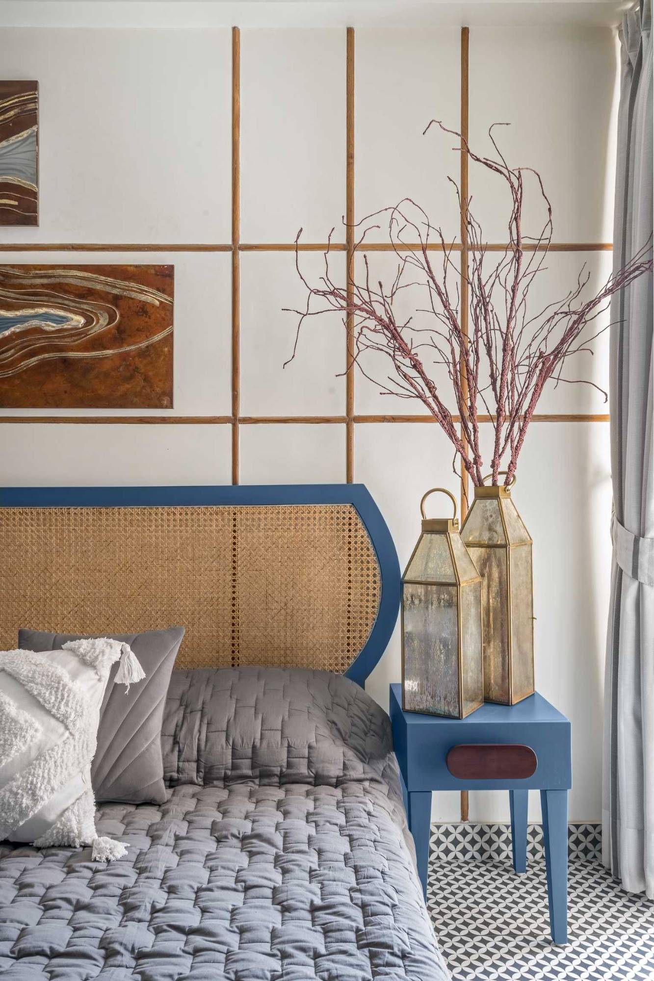 Bed with a blue-framed cane headboard, a blue bedside table with brass lanterns and a gridded timber wall