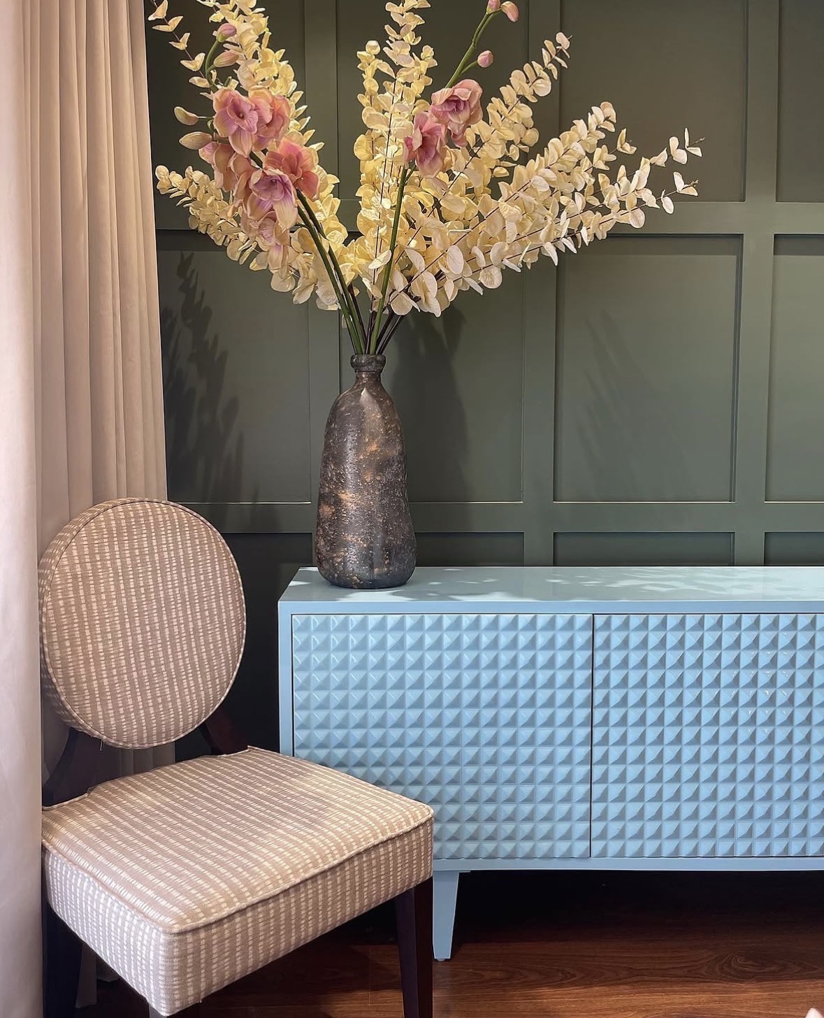 Pale blue relief sideboard against a green panelled wall, with a vase of blossom and an oval-backed chair