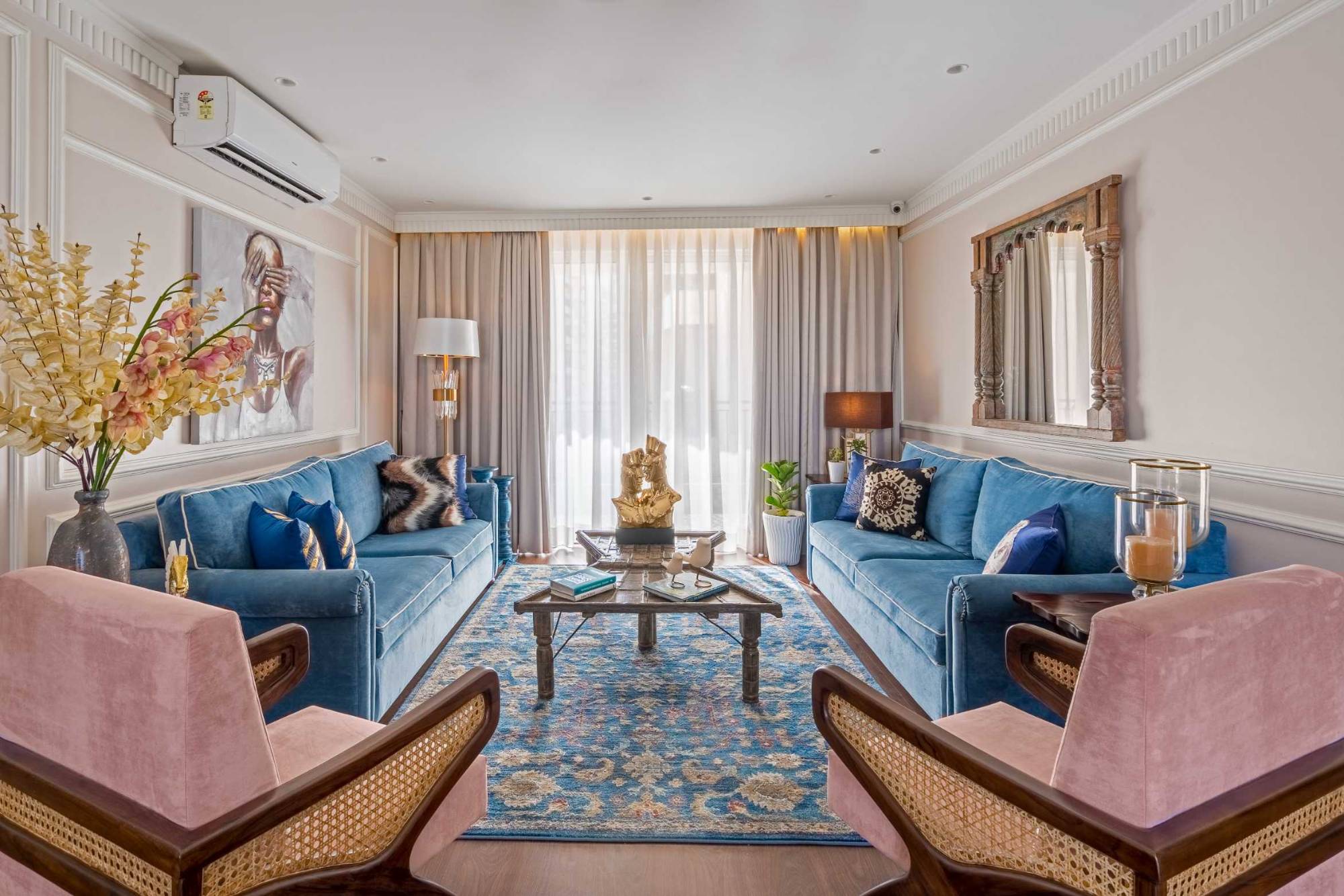 Living room seen across a pair of cane-armed blush chairs to two blue sofas, a coffee table and a curtained window