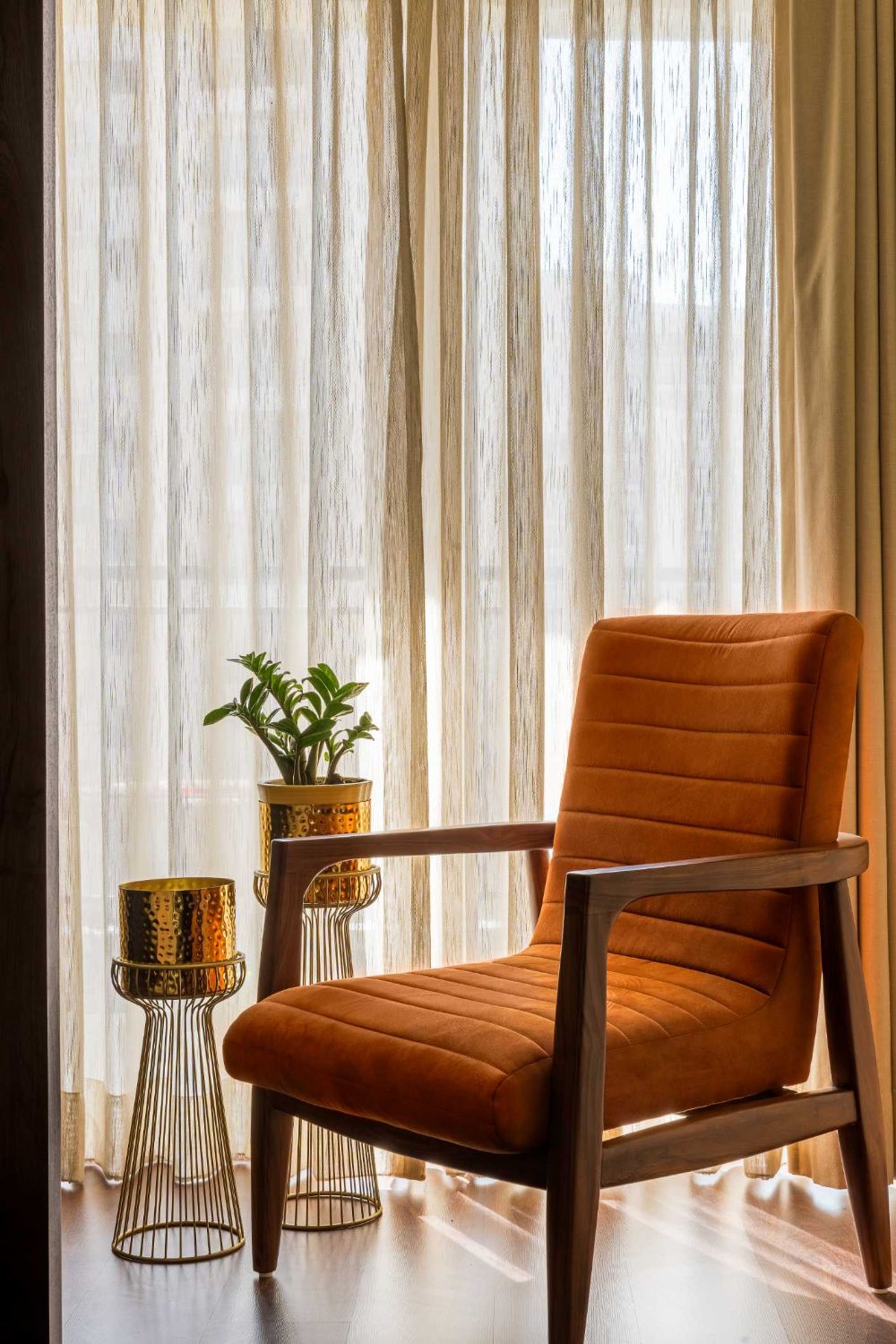 Rust-orange armchair in a window with sheer curtains and brass planters