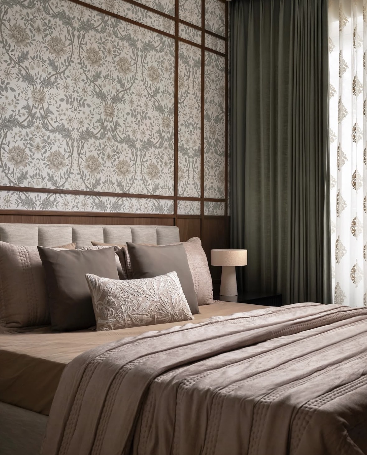 Bed with a channelled headboard against floral wallpaper held in timber battens, beside an olive curtain