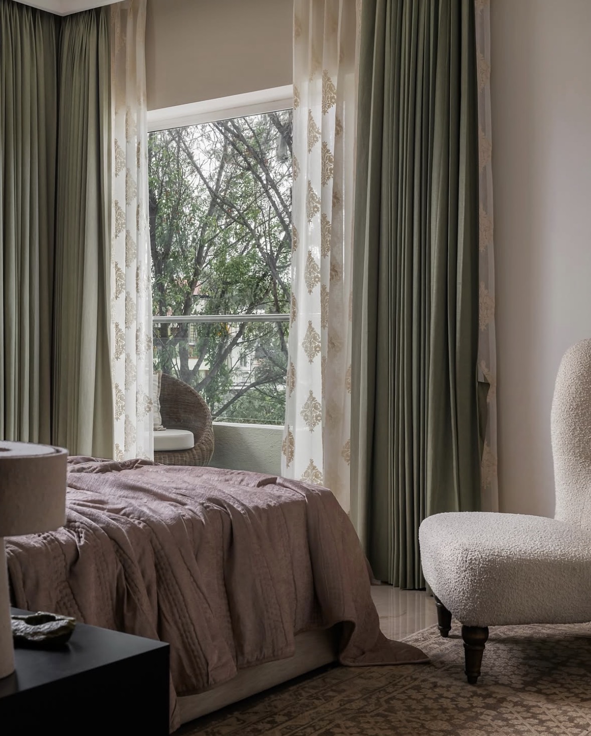 Bedroom with olive and embroidered sheer curtains, a rose throw on the bed and a boucle chair