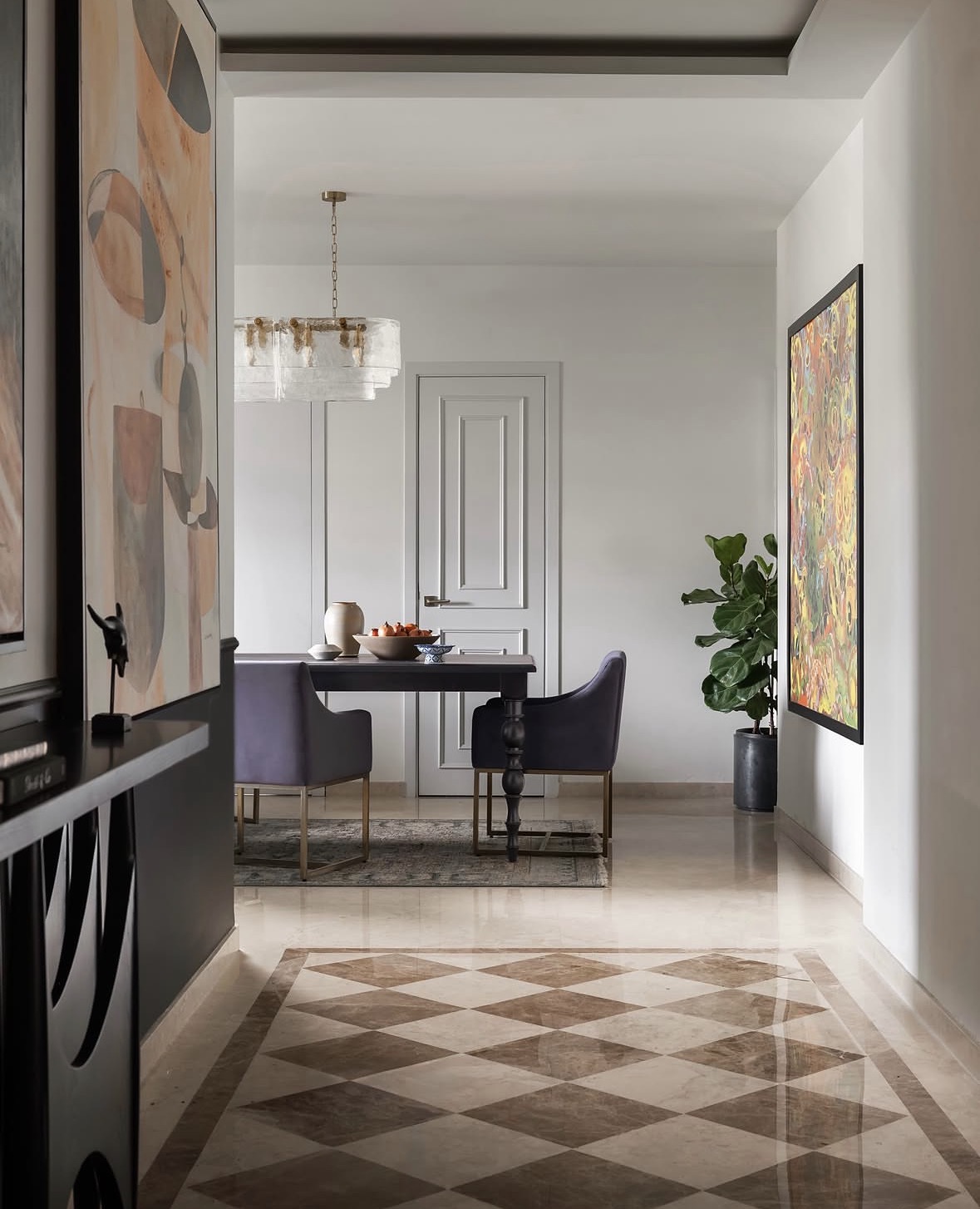 Chequered marble corridor with abstract paintings leading to a black dining table with plum chairs and a glass chandelier