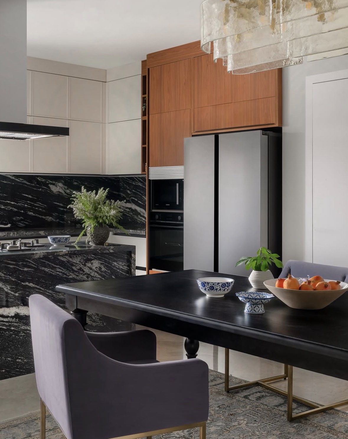 Kitchen with a timber tall unit and a black dining table with plum velvet chairs and a layered glass chandelier