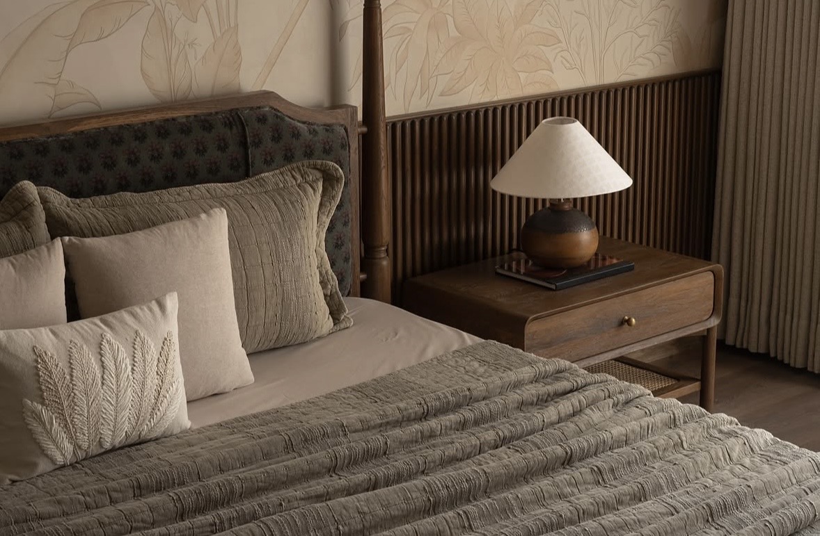 Four-poster bed with a patterned upholstered headboard, fluted timber panelling and a table lamp on the bedside table