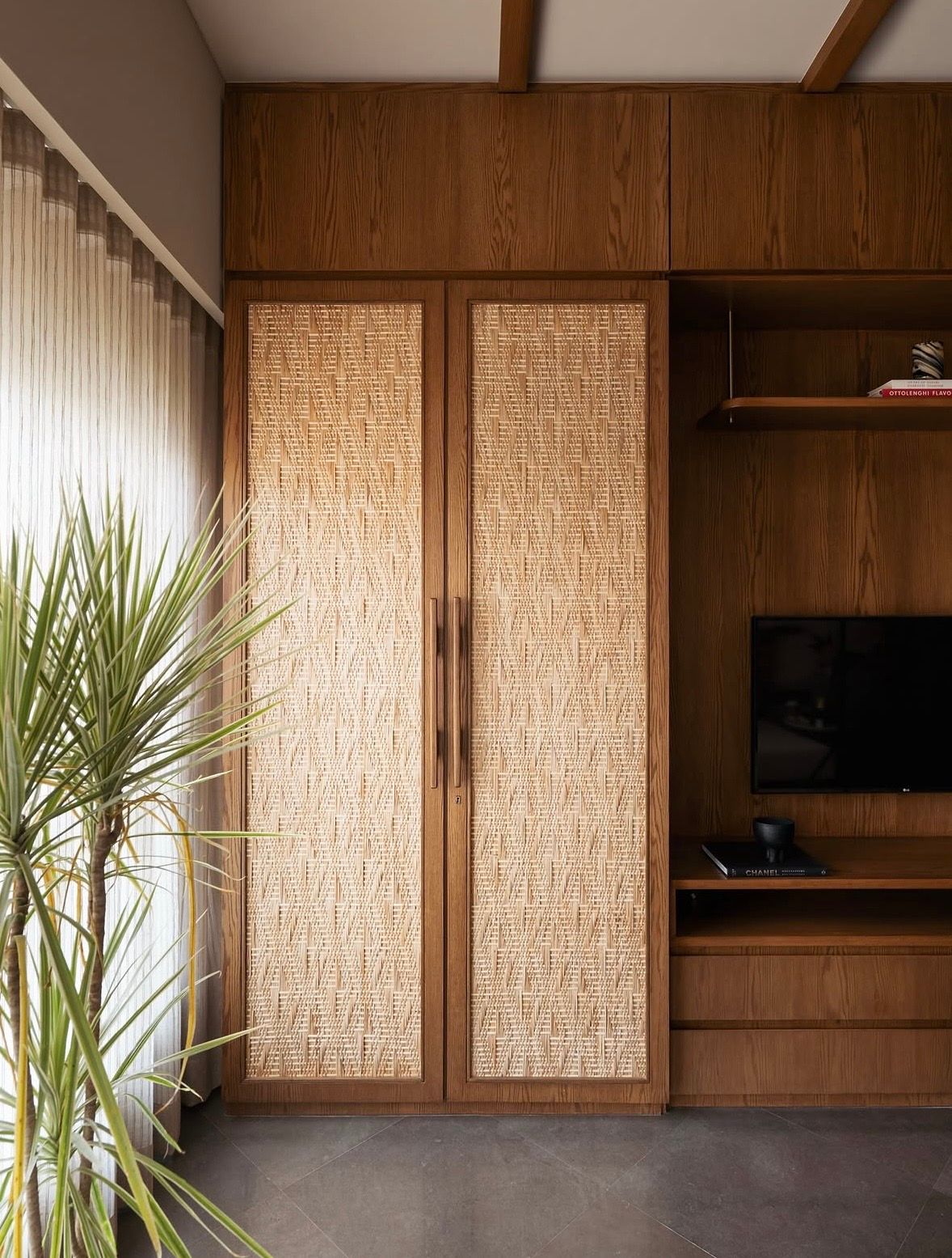 Timber wardrobe with woven panels beside a timber television unit and a tall plant