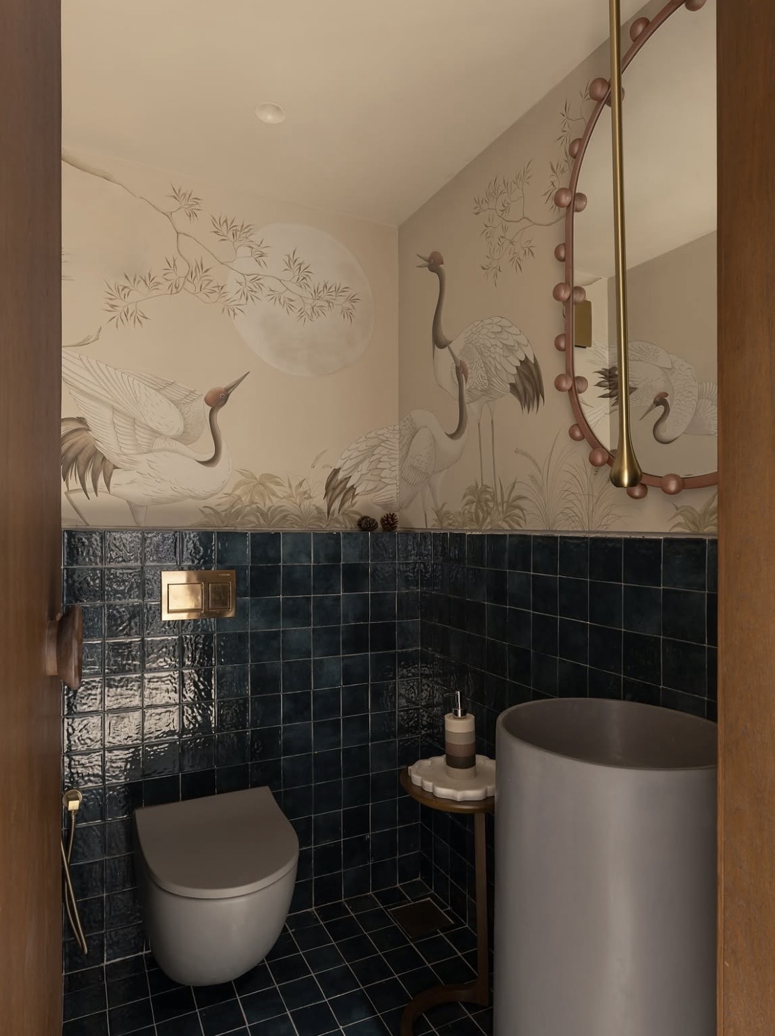 Powder room with crane wallpaper, deep blue tiles and a beaded oval mirror