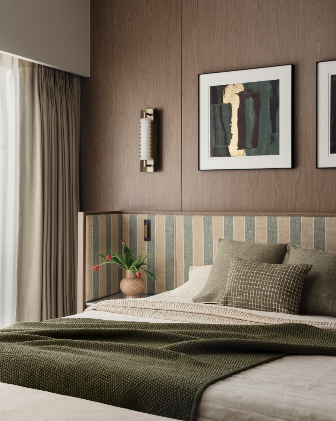 Bedroom with timber wall panelling, a brass wall light, framed art and a striped headboard with olive bedding