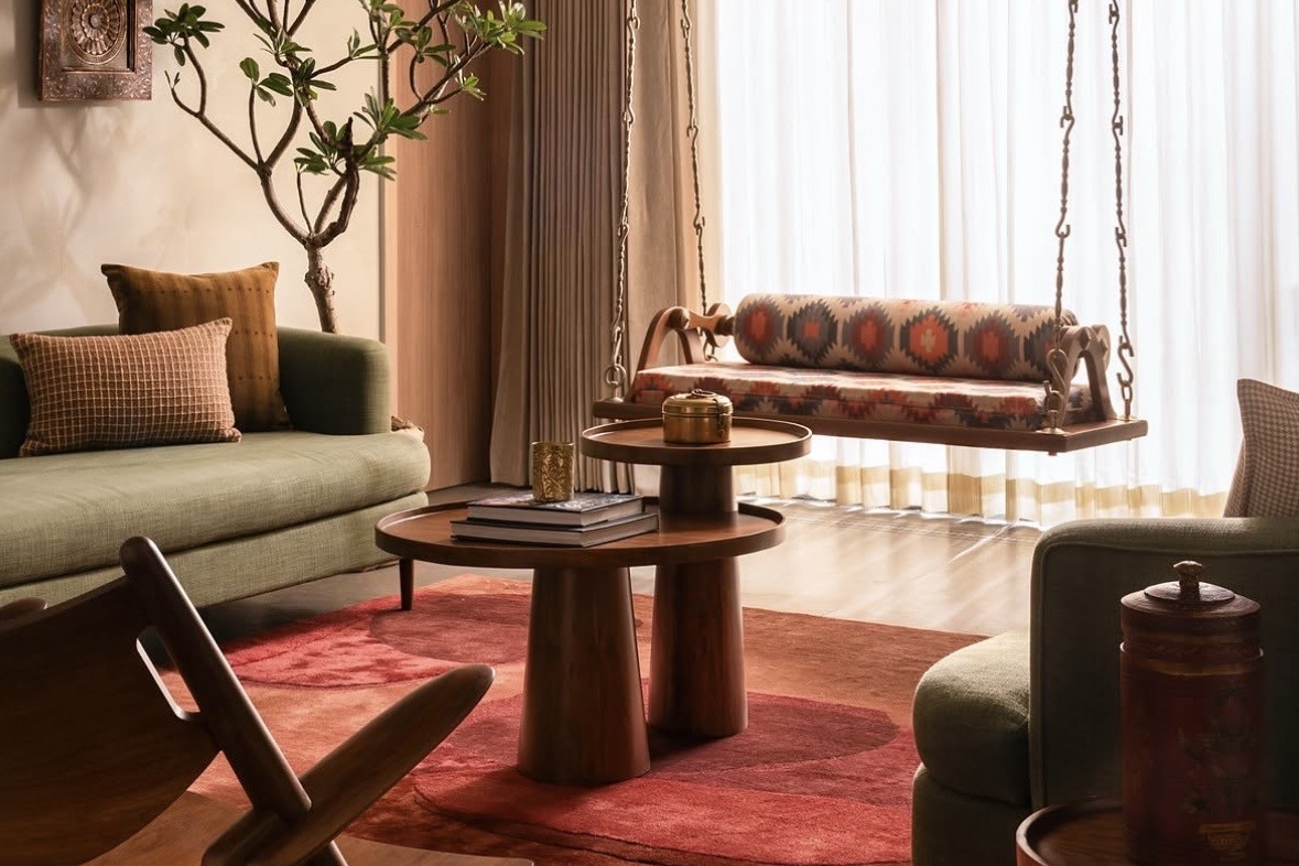 Living room with a carved swing in front of sheer curtains, a nest of round timber tables on a red rug and a green sofa