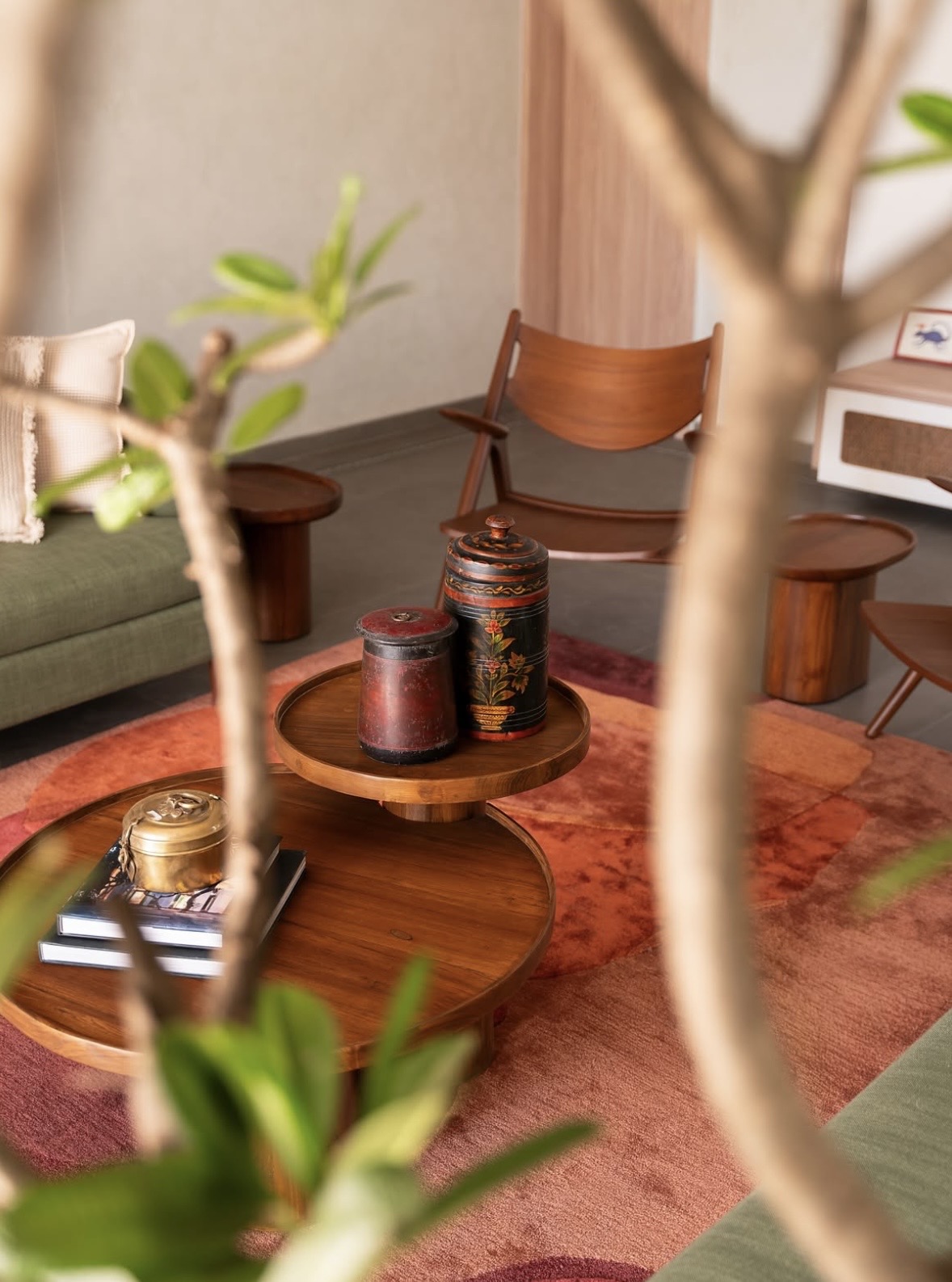 Painted wooden jars and a brass box on stacked round timber tables, seen through leaves