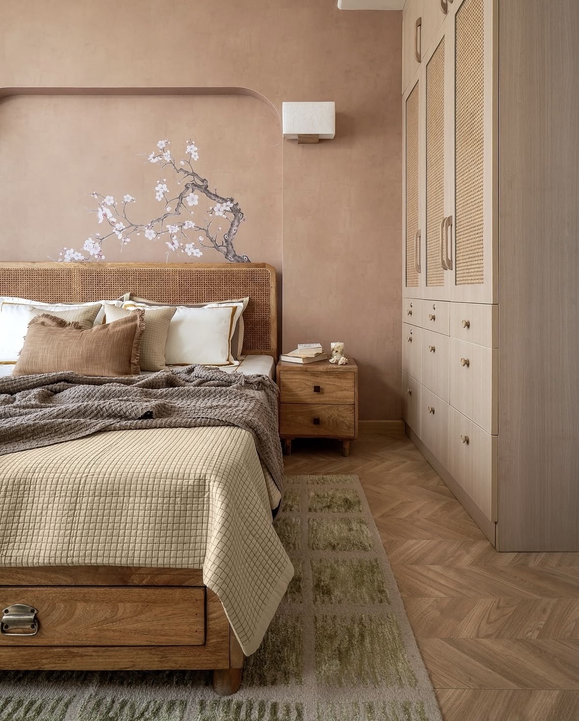 Blush bedroom with a cane headboard, a painted blossom branch above the bed and a wardrobe with woven cane doors