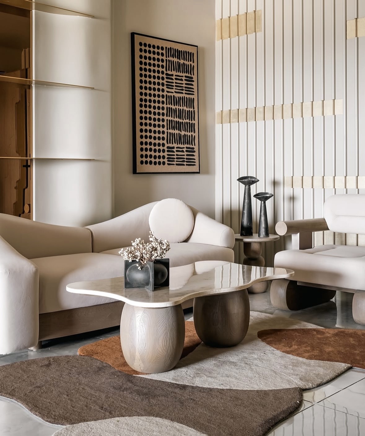 Cream curved sofa and a sculptural stone-topped coffee table on a rug in overlapping brown and sand shapes, with a tall fluted wall behind