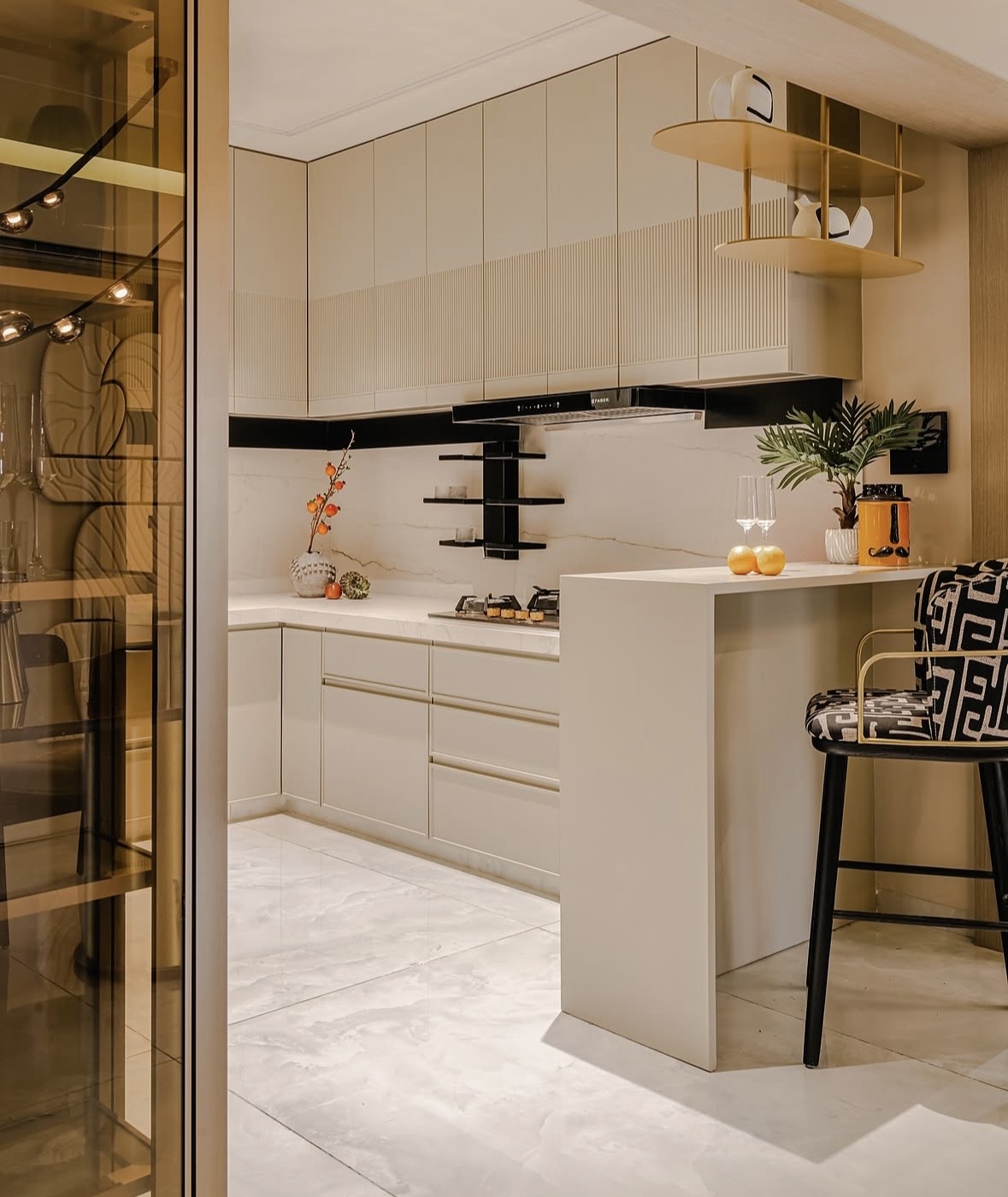 Kitchen with cream fluted-front cabinets, a stone-look backsplash, brass shelves and a breakfast counter with a patterned stool