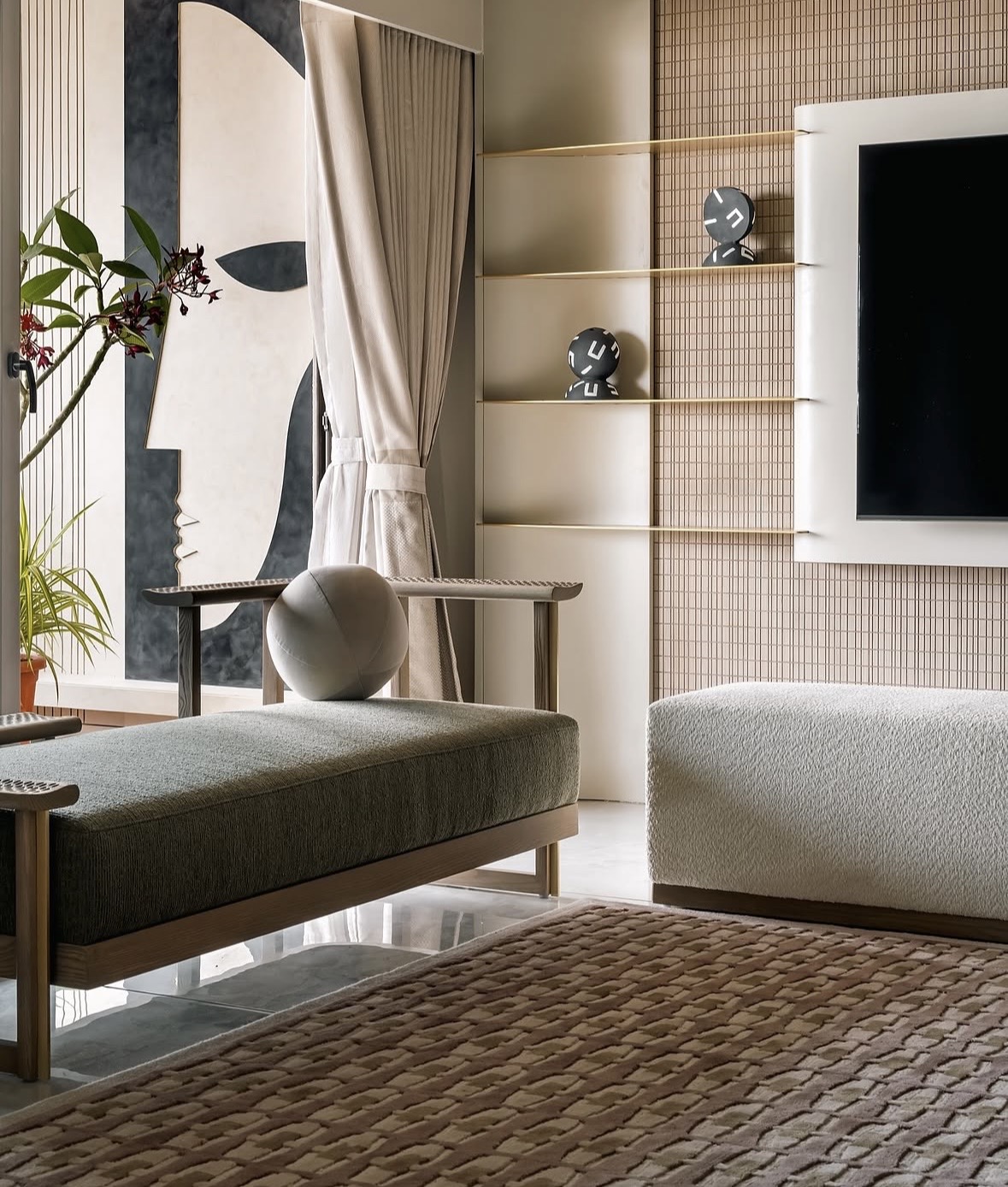 Daybed with a round cushion beside a mosaic-tiled media wall with brass shelves, and an abstract profile painting