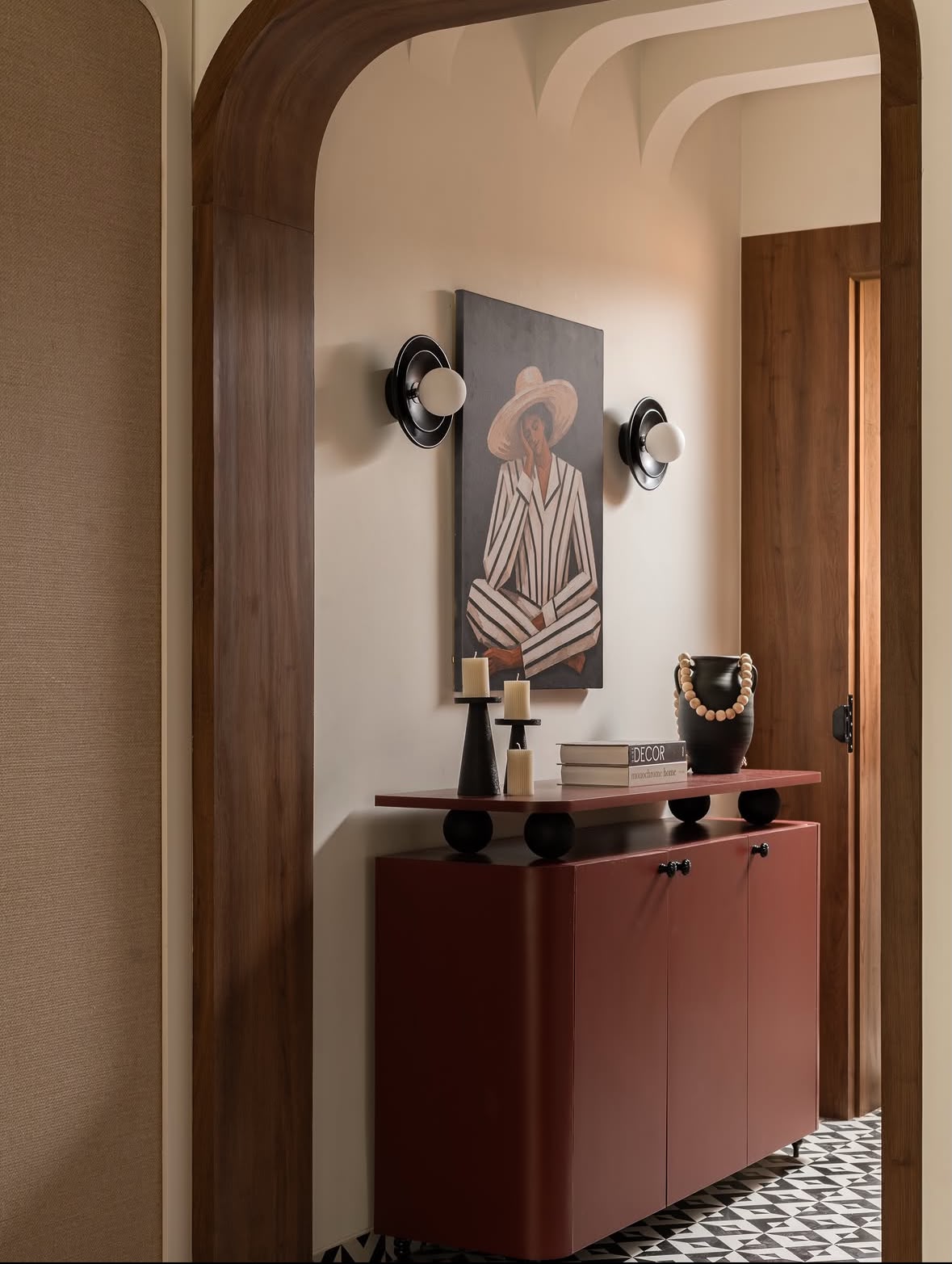 Arched entrance with a painted portrait, two wall lights and a rust-red console