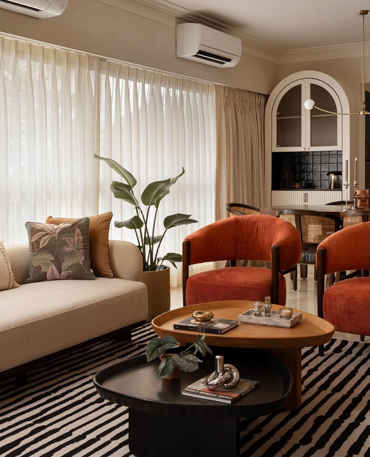 Living room with a striped rug, rust armchairs and a rounded wooden coffee table