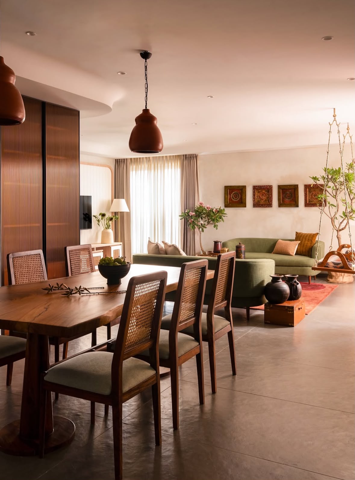 Dining table and sofa in an open living space lit by terracotta pendant lights