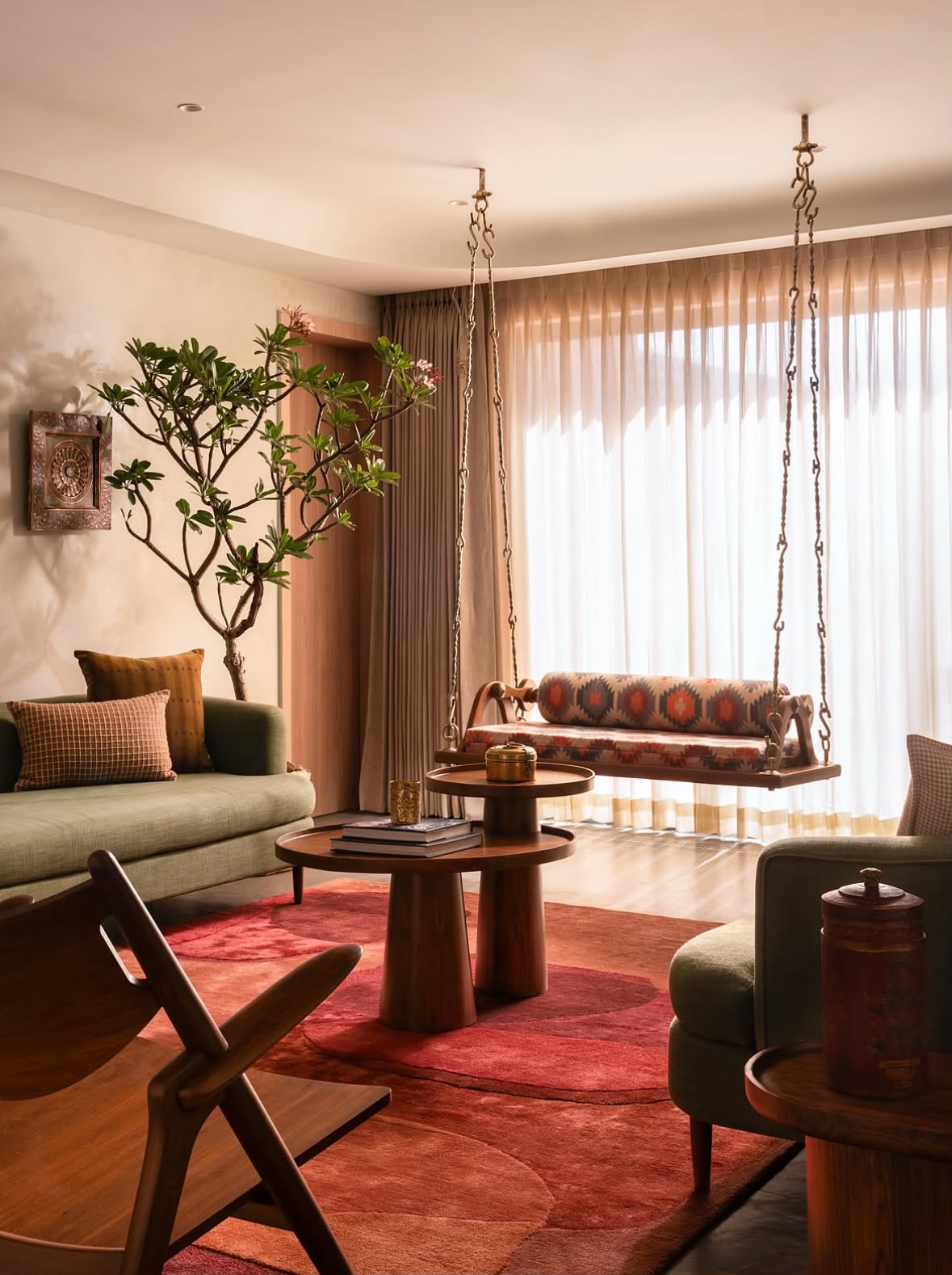 Living room with a green sofa, a wooden swing by sheer curtains and a flowering tree