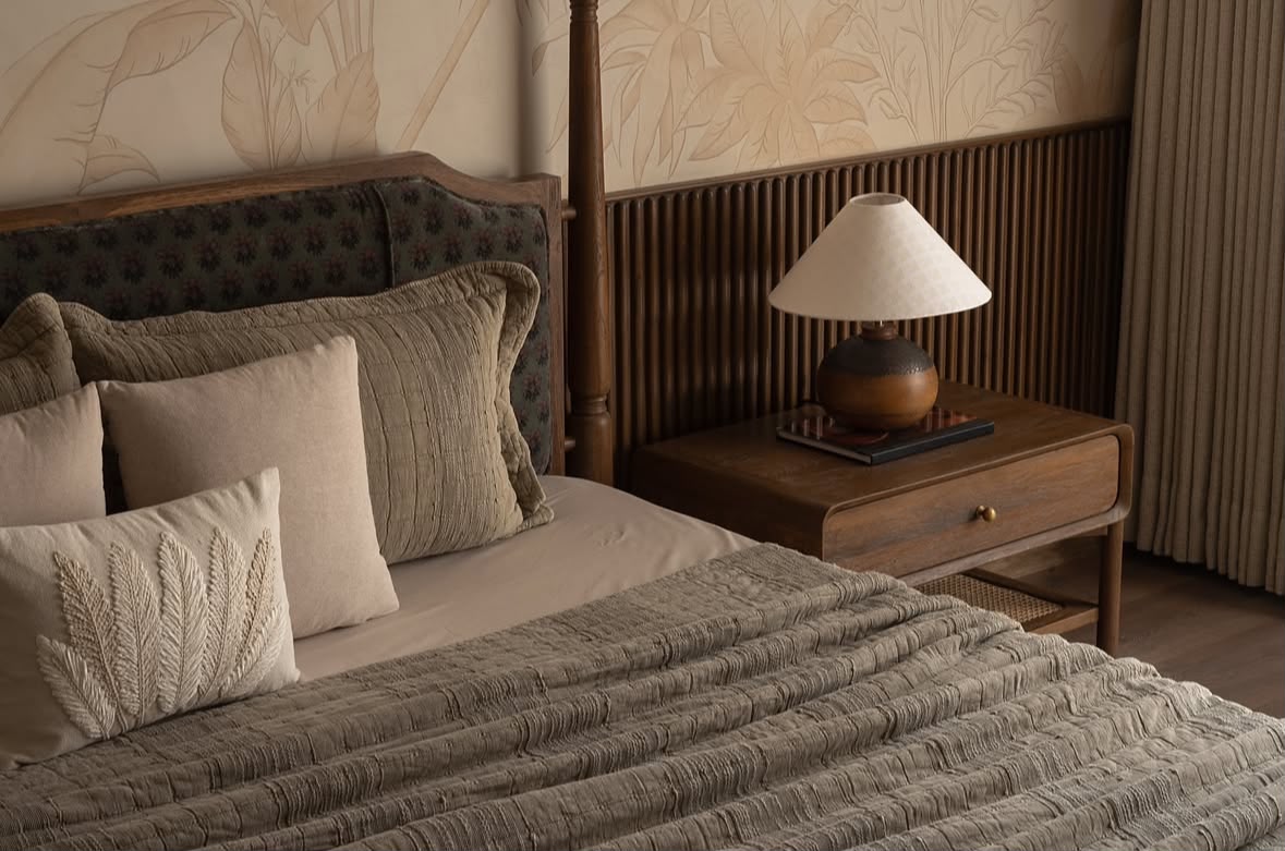 Bedroom with a button-tufted headboard, olive and stone bedding and a table lamp on a walnut bedside
