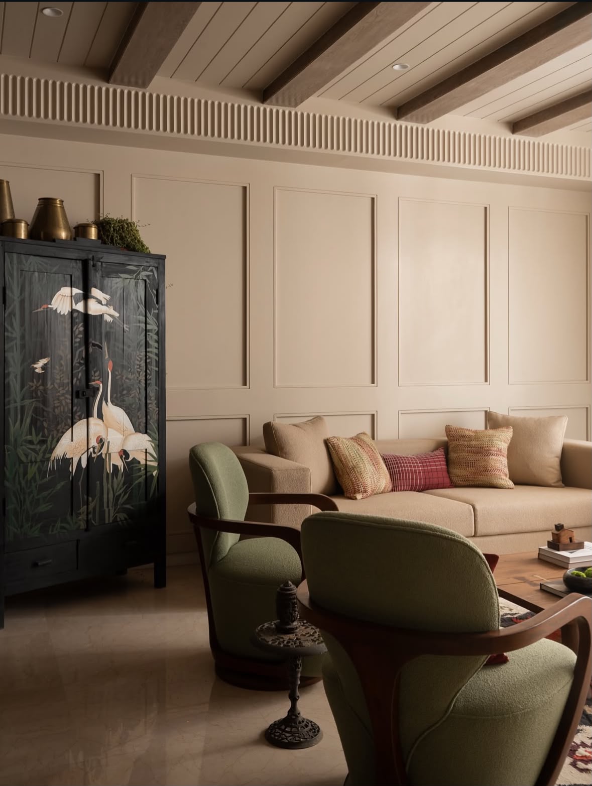 Living room with a black cabinet painted with white cranes, a beige sofa and green armchairs