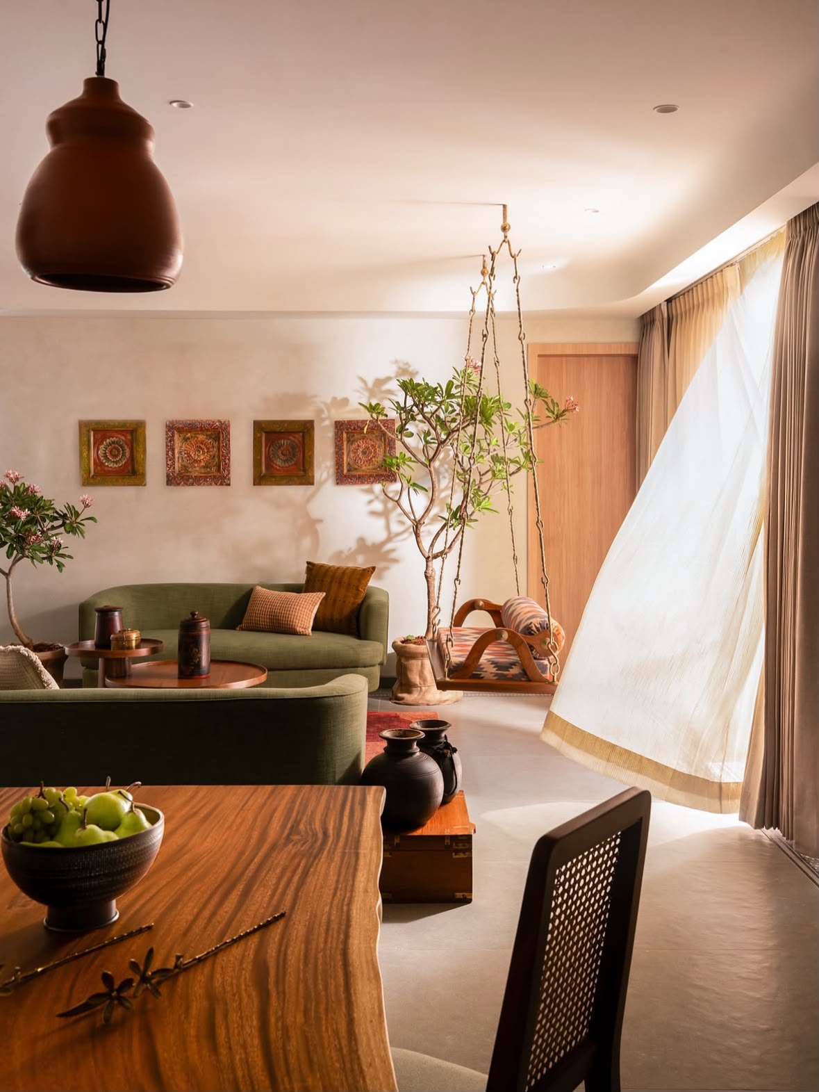 Sheer curtains moving in daylight beside a wooden dining table and a hanging swing