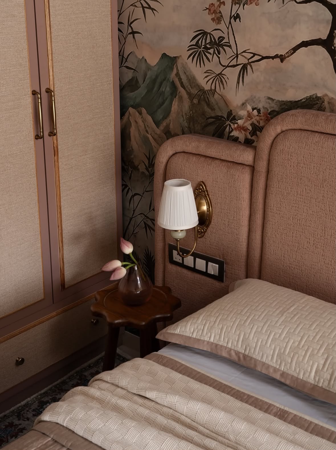 Brass wall light, a lotus in a glass vase and a painted landscape wallpaper beside an upholstered headboard